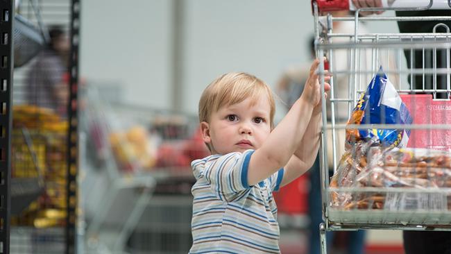 Ein Kleinkind hält sich an einen befüllten Einkaufswagen fest.