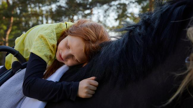 Ein Kind sitzt am Rücken eines schwarzen Pferdes und lehnt sich an.